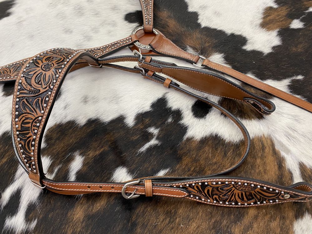 Leather headstall and breast collar with floral tooling on a cowhide rug